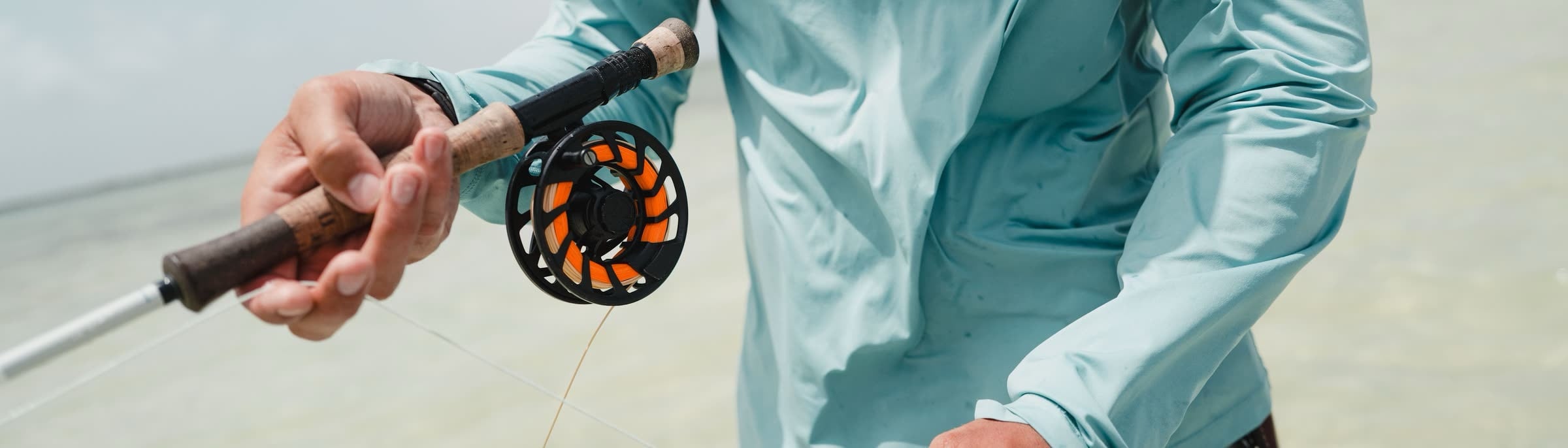 A fly reel and rod in an angler's hands on the water