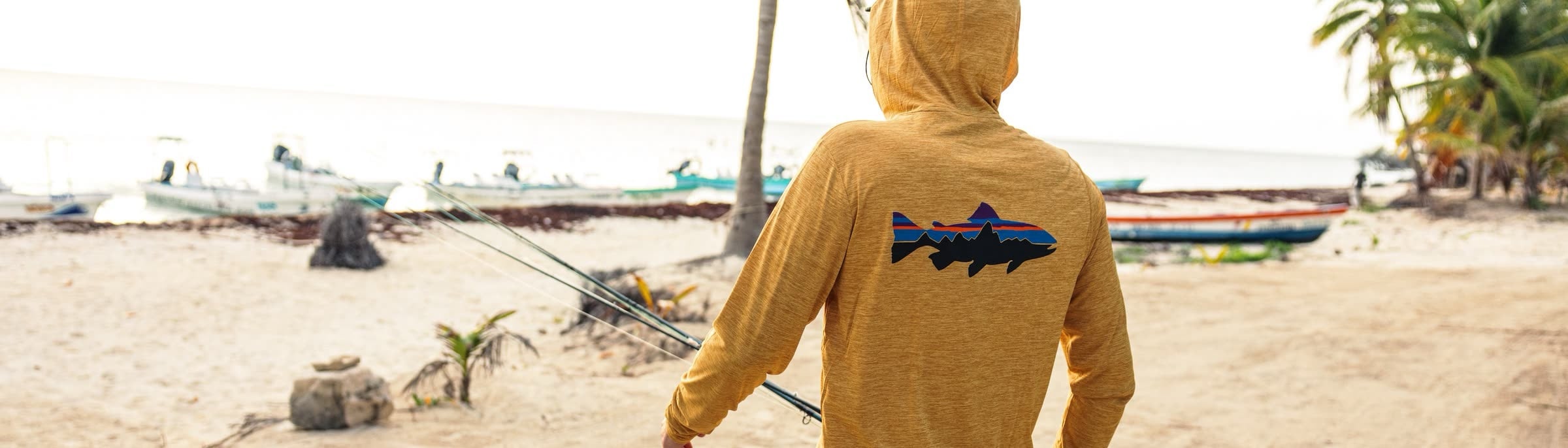An angler in a hooded sun shirt on a tropical beach