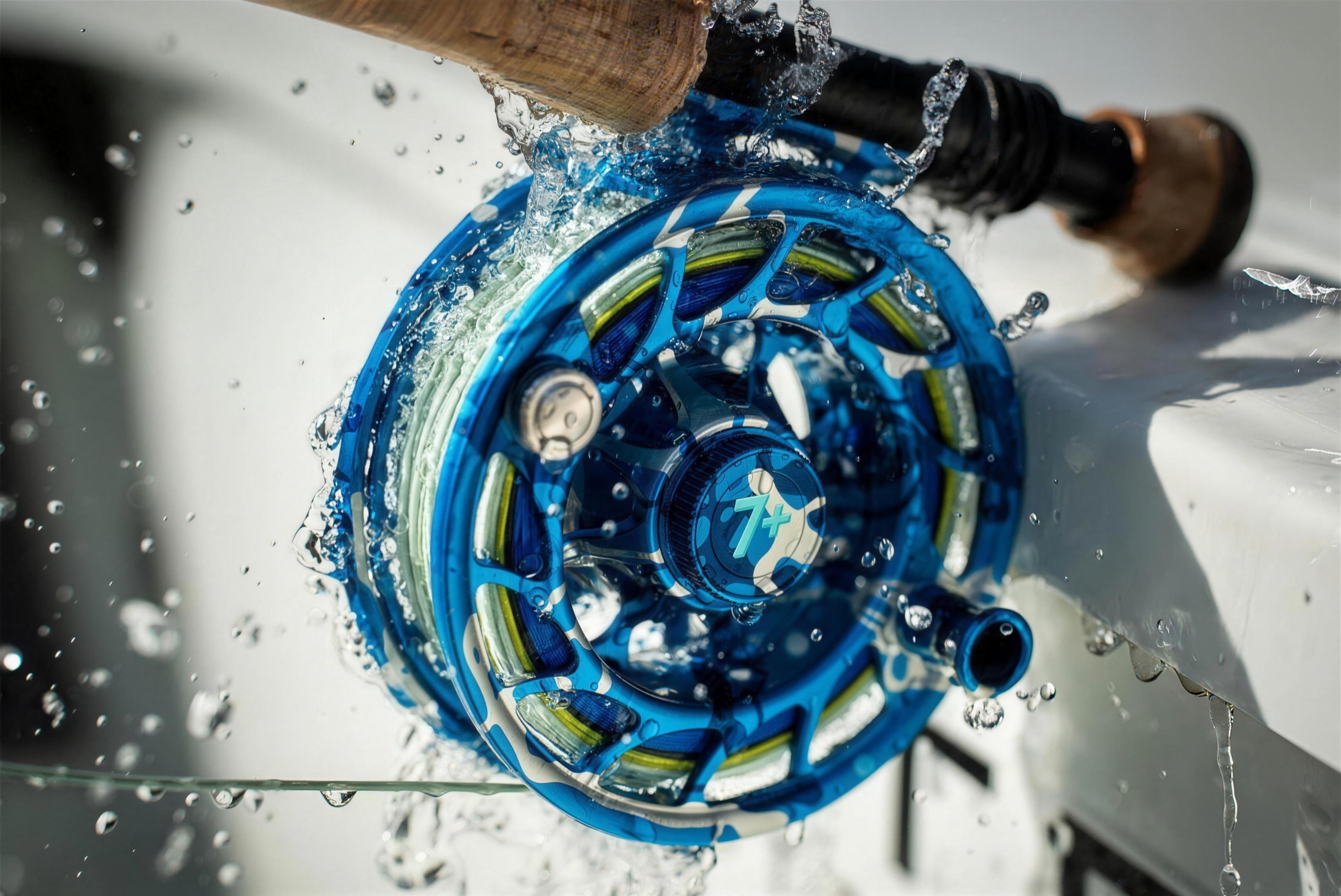 A Hatch Iconic 7 Plus reel in Splash Camo, water splashing off it on a boat gunwale